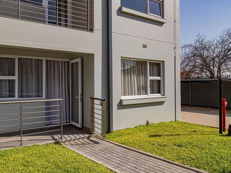 Ground floor apartment exterior featuring a paved walkway, small private lawn, and a tiled patio area with stainless steel balustrades.