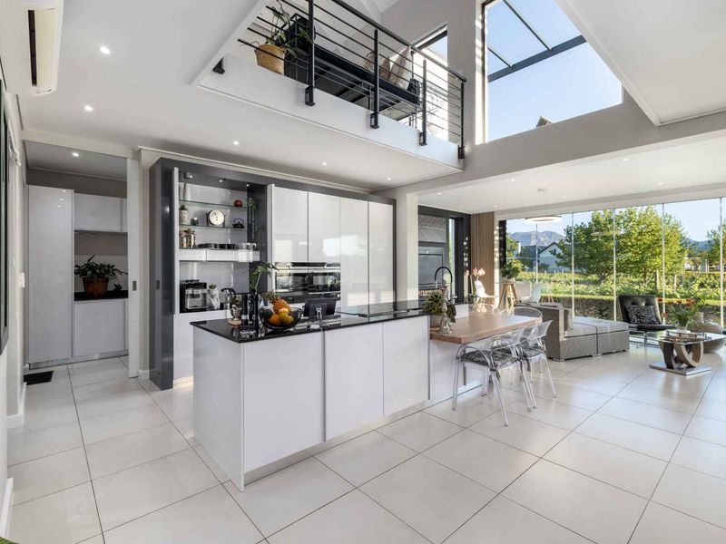 Modern open-plan living area featuring a sleek kitchen with island, high ceilings, mezzanine level, and expansive glass windows overlooking the garden.