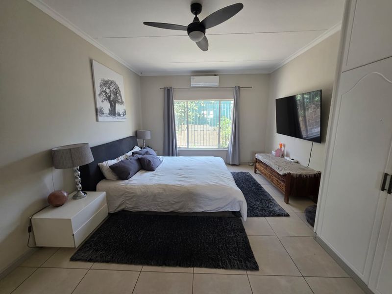 Spacious bedroom featuring tiled flooring, a ceiling fan, split-system air conditioning, and a built-in wardrobe with security bars on the window.