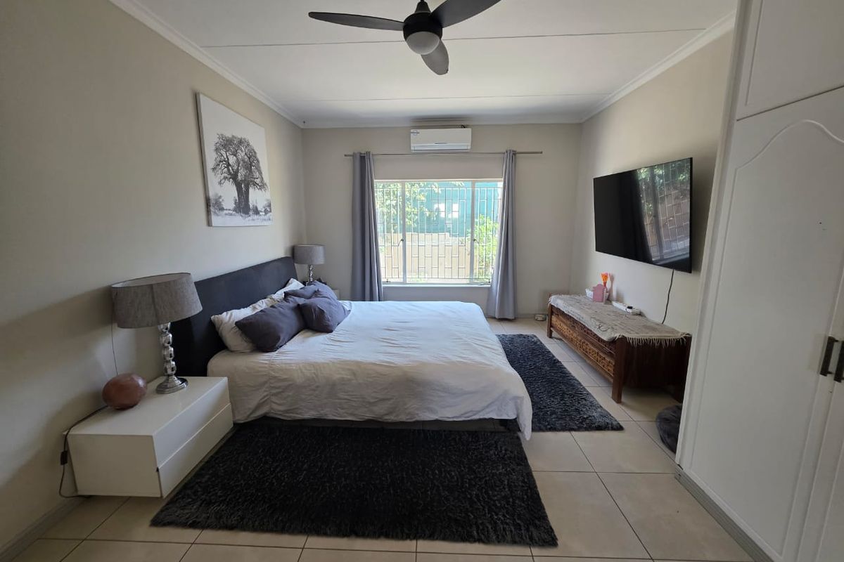 Spacious bedroom featuring tiled flooring, a ceiling fan, split-system air conditioning, and a built-in wardrobe with security bars on the window.