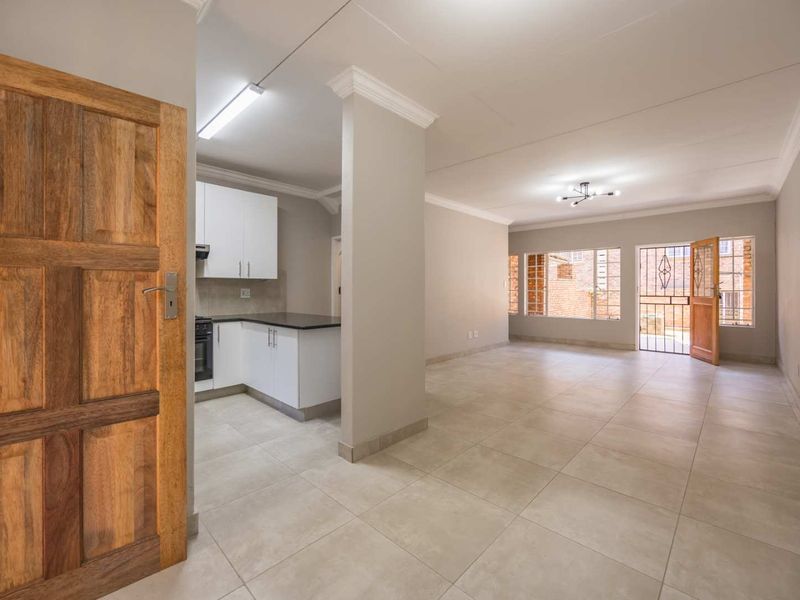 Spacious open-plan living area featuring neutral tiled flooring, modern kitchen cabinetry with stone countertops, and direct access to the exterior through a security gate.