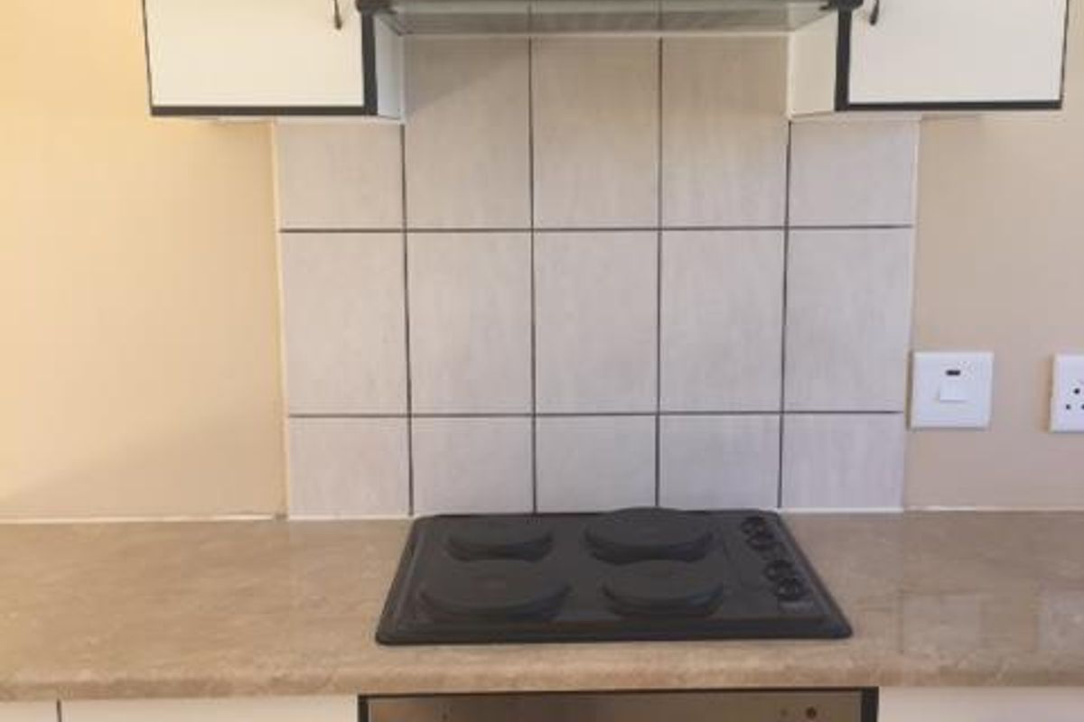 A functional kitchen area featuring white cabinetry, a stone-look countertop, tiled backsplash, and a built-in electric oven and hob with an extractor fan.