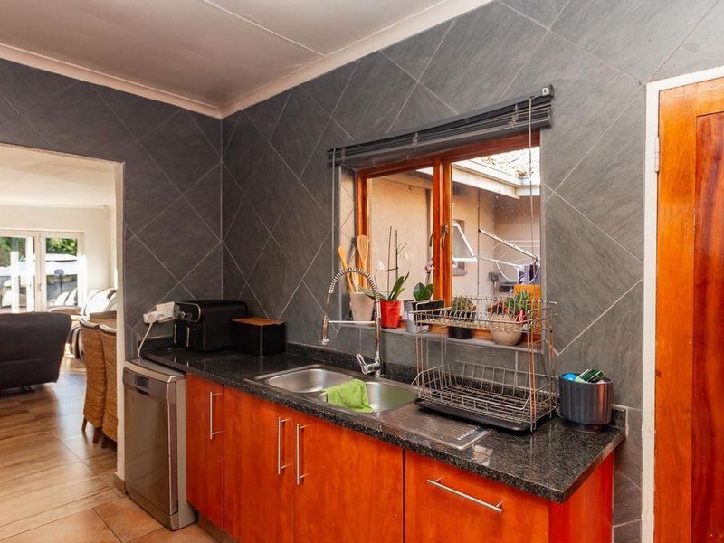 A functional kitchen featuring granite countertops, double basin sink, and wooden cabinetry, with a view through to the adjacent living area.