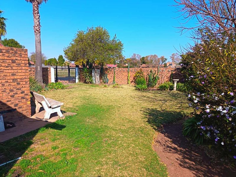A private backyard garden featuring a well-maintained lawn, established trees, and a secure brick boundary wall with a metal access gate.