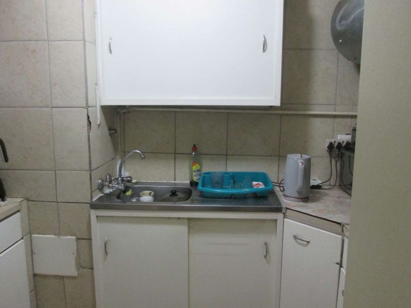 A compact kitchen area featuring a stainless steel sink, tiled splashback, and basic white cabinetry with laminate countertops.
