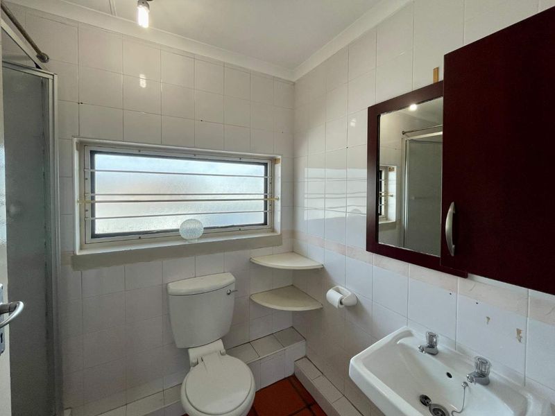 A compact bathroom featuring a shower enclosure, toilet, and washbasin with a wall-mounted mirror cabinet, finished with white wall tiles.