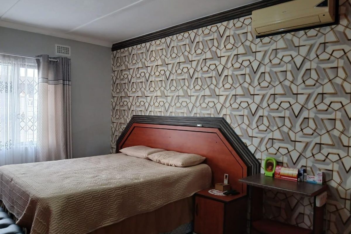 A bedroom featuring a patterned accent wall, built-in headboard with integrated bedside cabinetry, and a wall-mounted air conditioning unit.