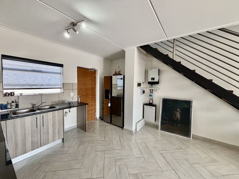 Modern kitchen area featuring herringbone tile flooring, double sink, and integrated inverter and battery storage system, adjacent to an internal staircase.
