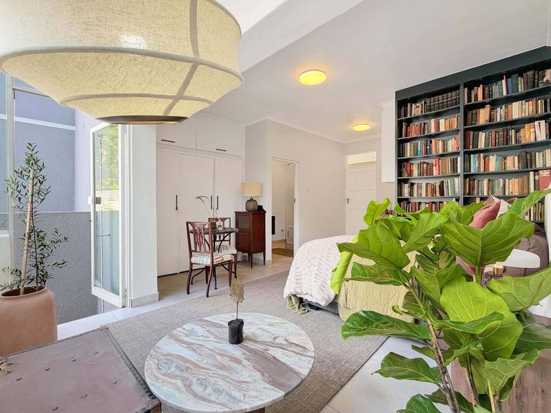 A well-lit bedroom featuring built-in cupboards, a large floor-to-ceiling bookshelf, and direct access to an outdoor area through a glass sliding door.