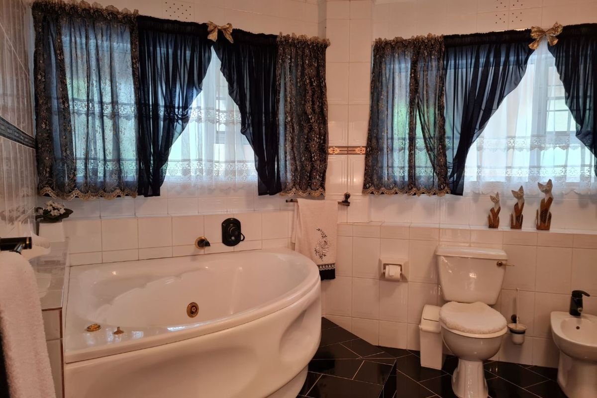 A dated bathroom featuring a corner jetted bathtub, a standard toilet, and a bidet, finished with white wall tiles and black floor tiles.