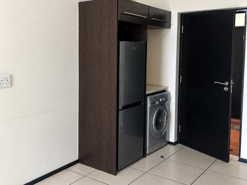 A clean, functional kitchen area featuring built-in dark wood cabinetry, tiled flooring, and space for integrated appliances.
