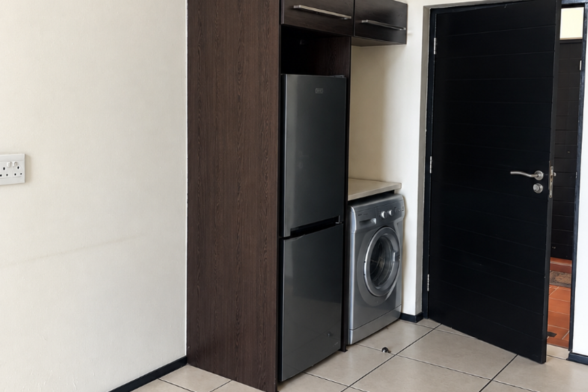 A clean, functional kitchen area featuring built-in dark wood cabinetry, tiled flooring, and space for integrated appliances.