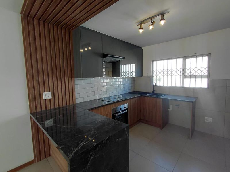 Modern kitchen featuring dark cabinetry, marble-look countertops, subway tile backsplash, built-in oven and hob, and a decorative timber slat wall feature.
