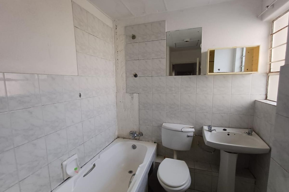 A dated bathroom featuring a bathtub, pedestal basin, and toilet, requiring renovation due to missing tiles and worn finishes.