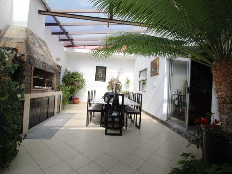 Covered patio area featuring a built-in braai, tiled flooring, and a translucent roof, providing a versatile space for outdoor dining and entertainment.