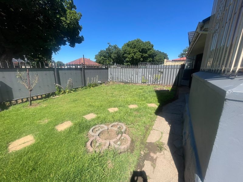 A rear garden area featuring a lawn, stone pathway, and perimeter fencing with security razor wire.