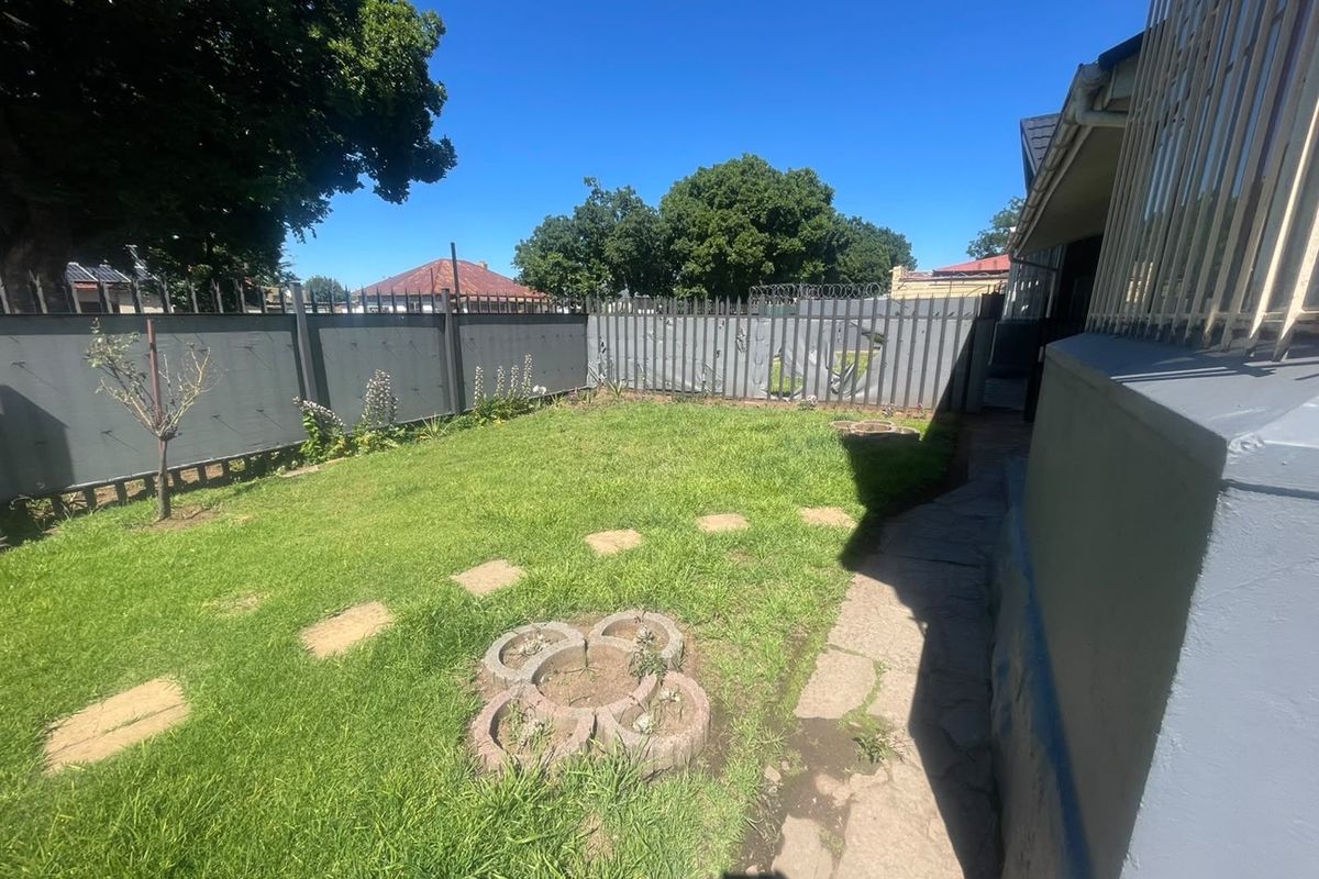 A rear garden area featuring a lawn, stone pathway, and perimeter fencing with security razor wire.