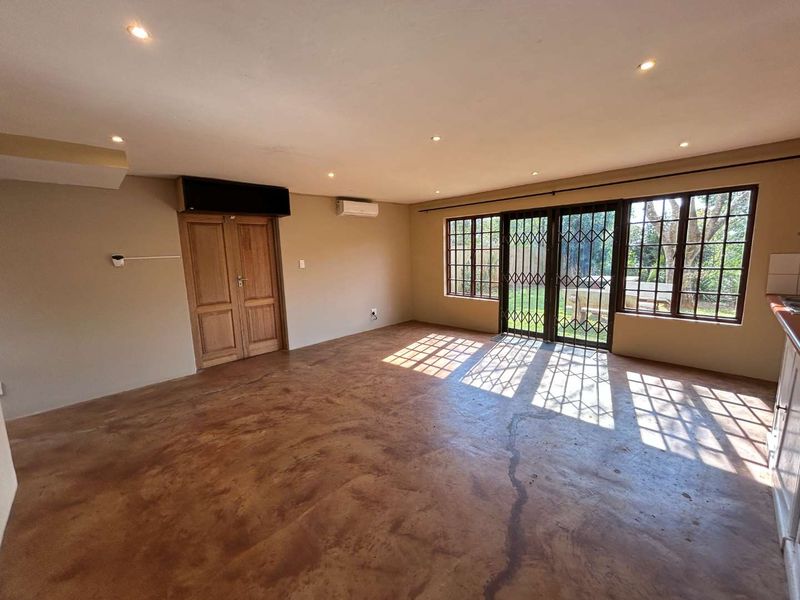 Spacious open-plan living area featuring polished concrete floors, recessed lighting, split-system air conditioning, and direct access to the garden through secure metal-framed doors.