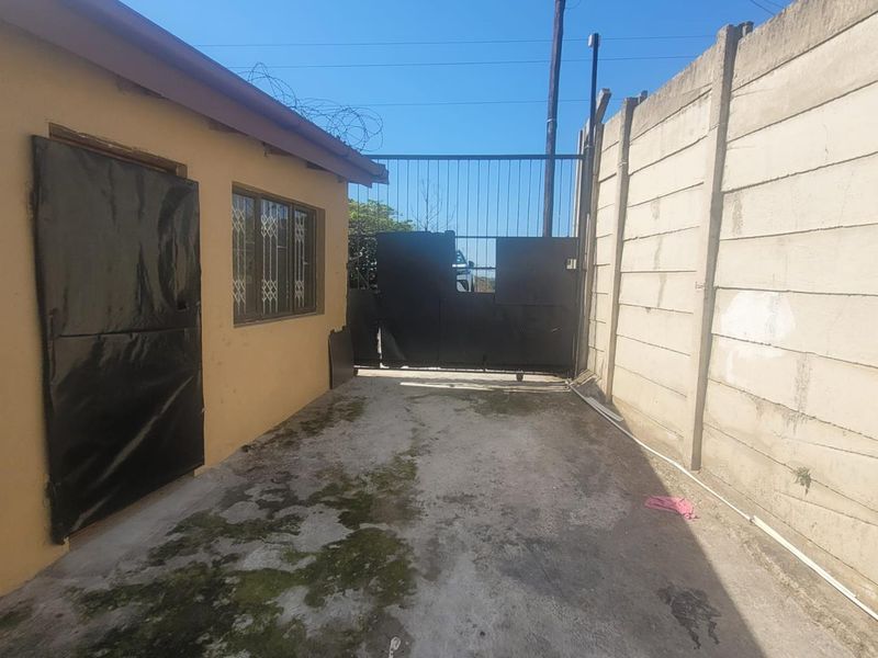 A rear exterior view of the cottage featuring a concrete driveway, a metal security gate, and perimeter precast concrete walling.