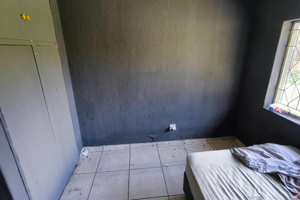 A bedroom featuring dark painted walls, tiled flooring, and built-in cupboard storage with a security-barred window.