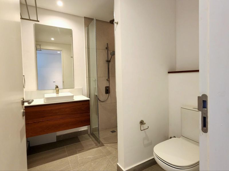 Modern bathroom featuring a floating wood-veneer vanity, vessel sink, glass-enclosed walk-in shower with rainfall showerhead, and neutral floor tiling.