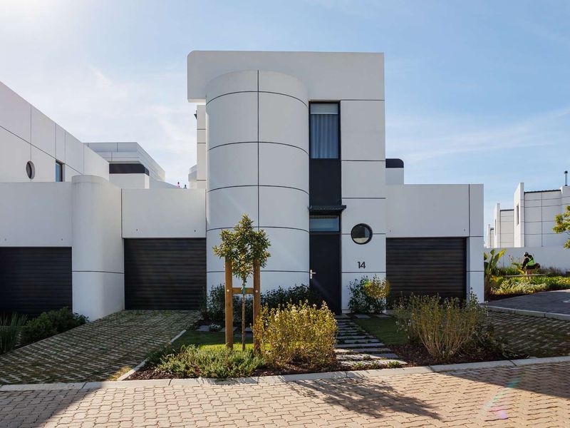 Modern architectural front elevation featuring a striking cylindrical design element, double garage, and neat landscaped garden with paved driveway.
