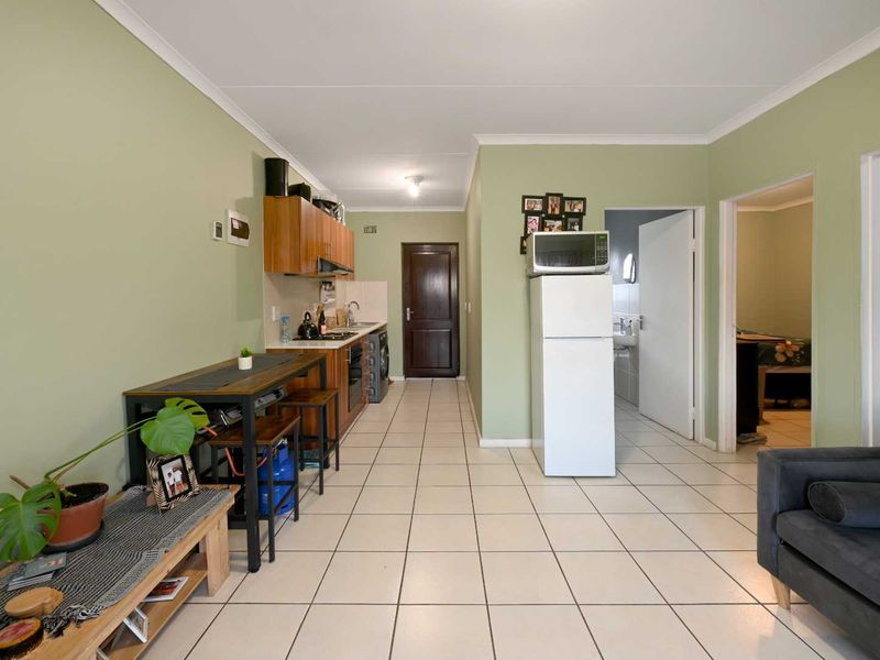 Open-plan living area featuring tiled flooring and a functional kitchen with built-in cabinetry, oven, and hob, leading to adjacent rooms.