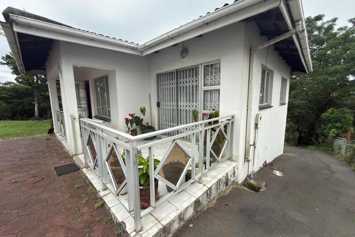Rear exterior view of the house featuring a tiled patio area with metal security gates and balustrades, overlooking the surrounding garden and driveway.