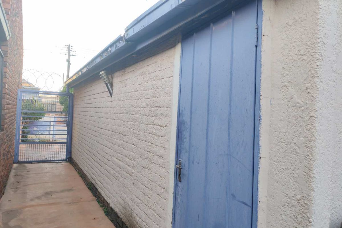 A side exterior view of the property featuring a textured masonry wall, a blue metal door, and a security gate leading to the rear area.