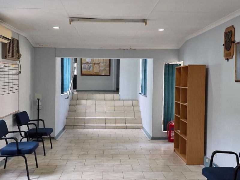 A functional office reception area featuring tiled flooring, a staircase leading to an upper level, and integrated air conditioning.