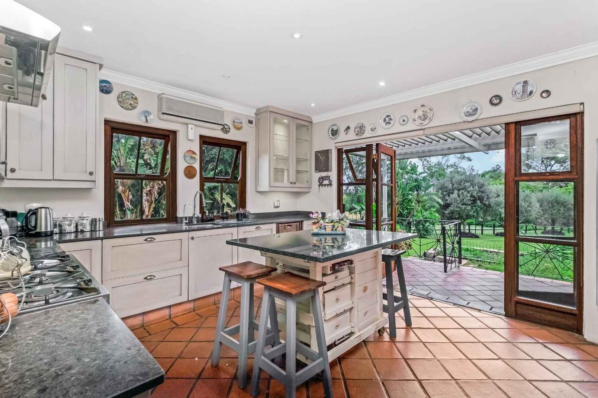 Spacious kitchen featuring granite countertops, gas cooktop, and terracotta flooring, with direct access to a covered outdoor patio area.