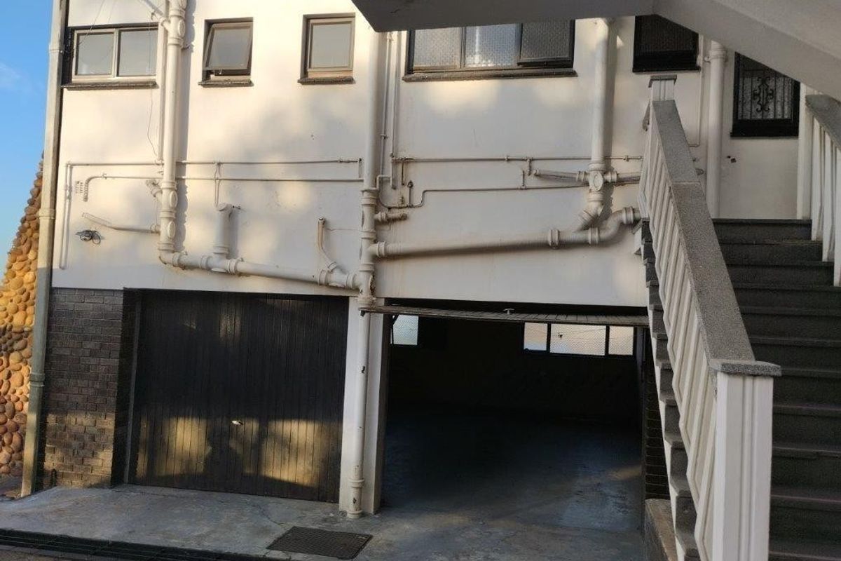 Rear exterior view of the property featuring a garage, external staircase, and exposed plumbing along the building facade.