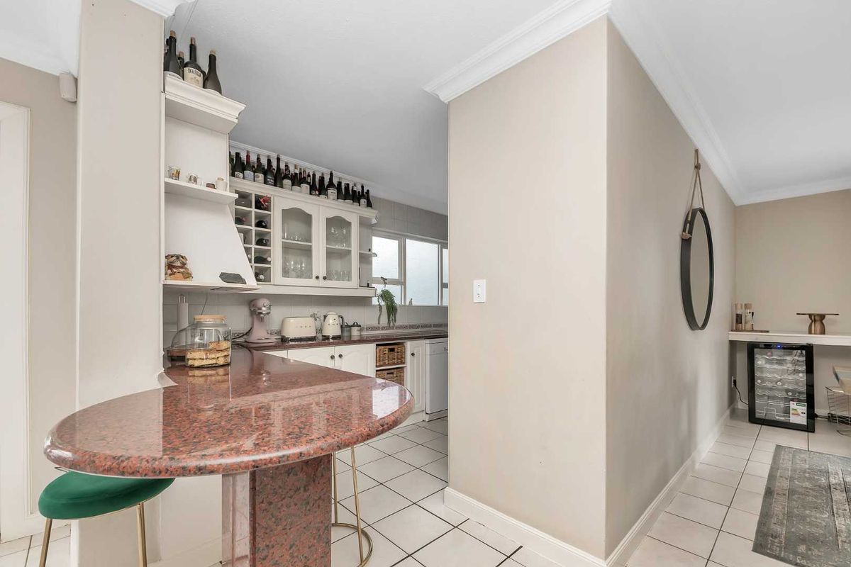 A functional kitchen featuring granite countertops, white cabinetry, and tiled flooring, with an adjacent breakfast bar and integrated wine cooler.