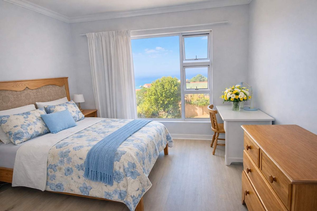 A bright bedroom featuring light wood-look flooring, neutral walls, and a large window offering scenic coastal views.
