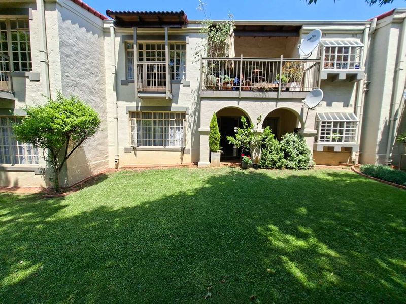 Rear view of the townhouse featuring a private garden, a covered patio with arched entry, and an upper-level balcony with metal railings.