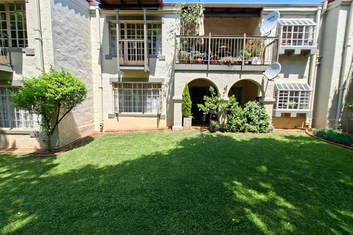 Rear view of the townhouse featuring a private garden, a covered patio with arched entry, and an upper-level balcony with metal railings.