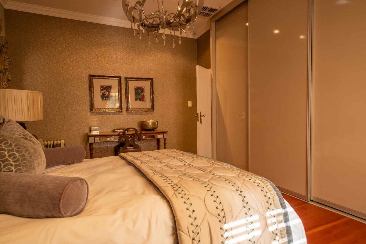 A well-maintained bedroom featuring built-in sliding door wardrobes, textured wallpaper, and polished wooden flooring.
