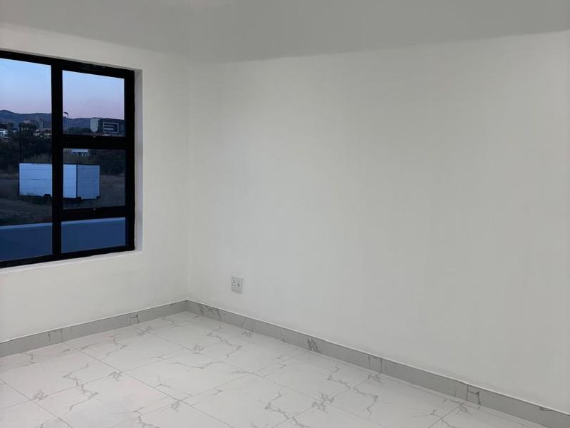 A bright, modern, and empty bedroom featuring high-quality marble-look floor tiles, recessed ceiling lighting, and a large black-framed window.