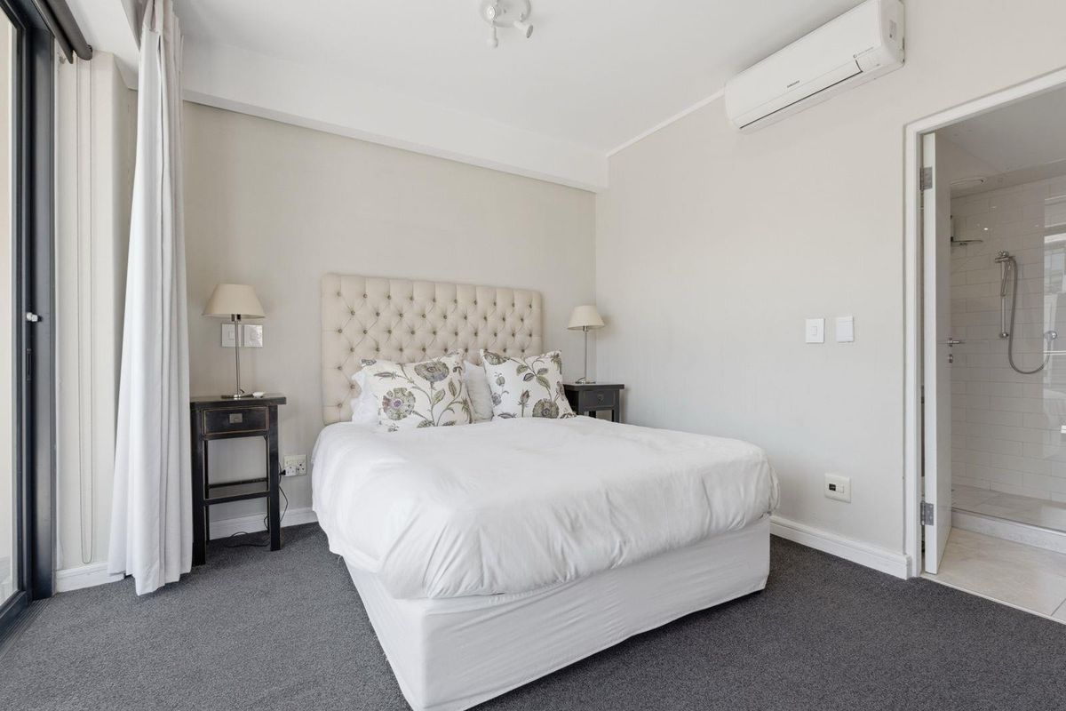 A well-maintained bedroom featuring neutral walls, carpet flooring, a split-system air conditioner, and direct access to an en-suite bathroom.