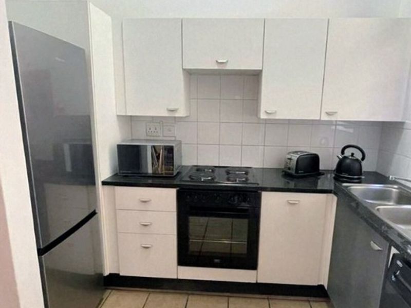 Compact kitchen featuring white cabinetry, black granite countertops, built-in oven, electric hob, and tiled flooring, providing a functional and efficient workspace.