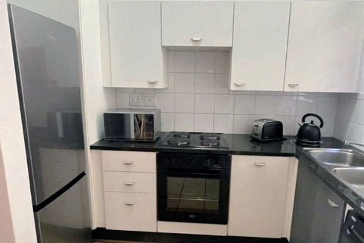 Compact kitchen featuring white cabinetry, black granite countertops, built-in oven, electric hob, and tiled flooring, providing a functional and efficient workspace.