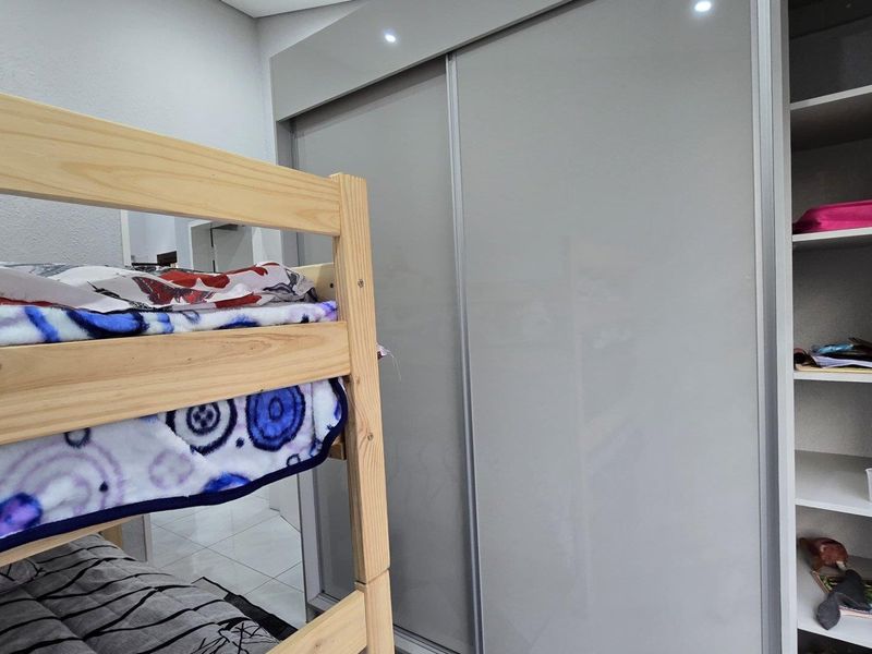A bedroom featuring a modern grey built-in sliding door wardrobe and an integrated open shelving unit with recessed ceiling lighting.