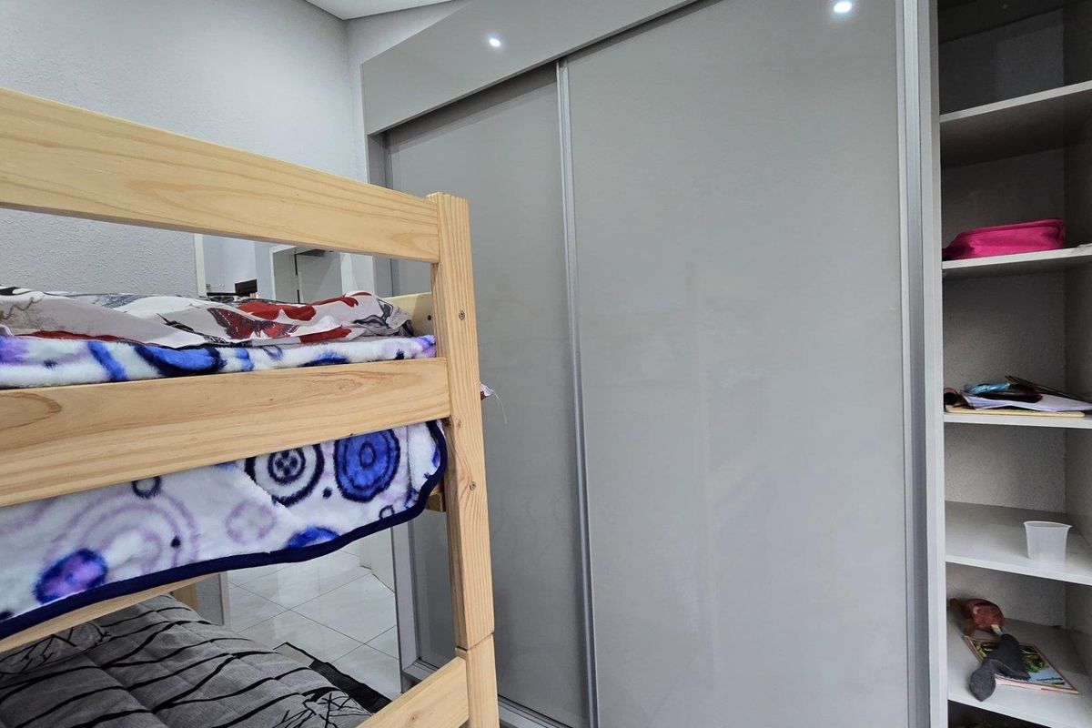 A bedroom featuring a modern grey built-in sliding door wardrobe and an integrated open shelving unit with recessed ceiling lighting.
