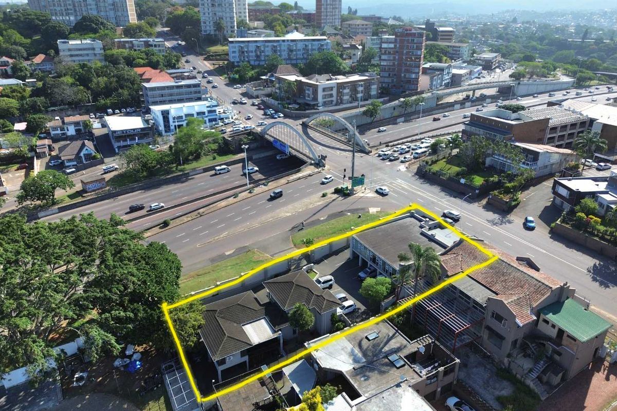 Aerial view of the commercial property highlighting the building layout, roof structure, parking area, and surrounding urban infrastructure.