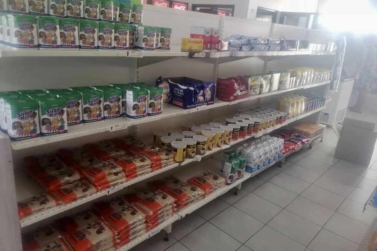 A retail space featuring rows of metal shelving units stocked with various grocery products and finished with tiled flooring.