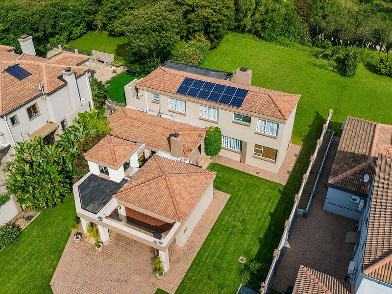 Aerial view of a residential property featuring a tiled roof with solar panels, a paved driveway, and a well-maintained lawn.