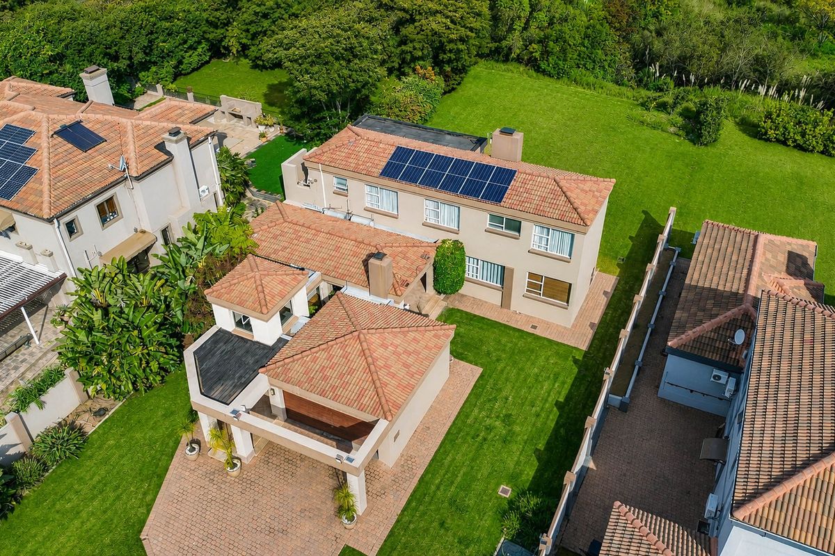 Aerial view of a residential property featuring a tiled roof with solar panels, a paved driveway, and a well-maintained lawn.