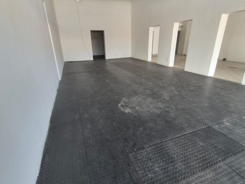 An empty, open-plan commercial space featuring durable rubber flooring, fluorescent lighting, and multiple access points, suitable for various business or retail applications.
