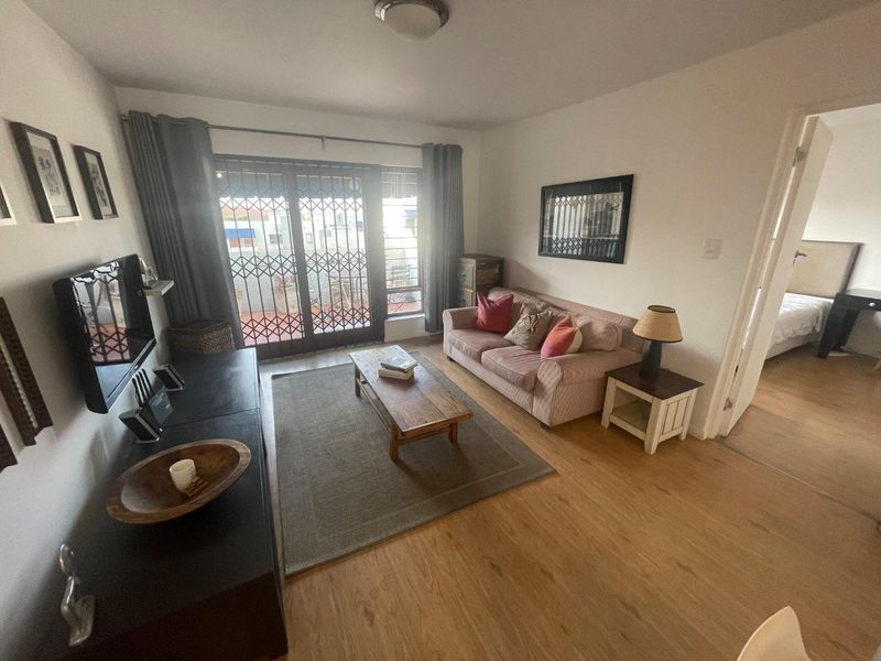 A comfortable living room featuring laminate flooring and a sliding glass door with a security gate, providing access to an outdoor area.