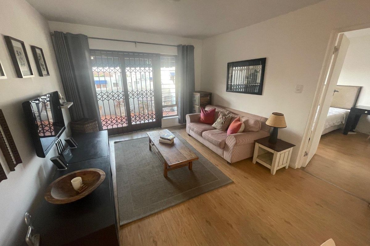 A comfortable living room featuring laminate flooring and a sliding glass door with a security gate, providing access to an outdoor area.
